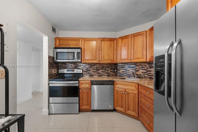 kitchen with sink, decorative backsplash, light stone countertops, light tile patterned floors, and stainless steel appliances