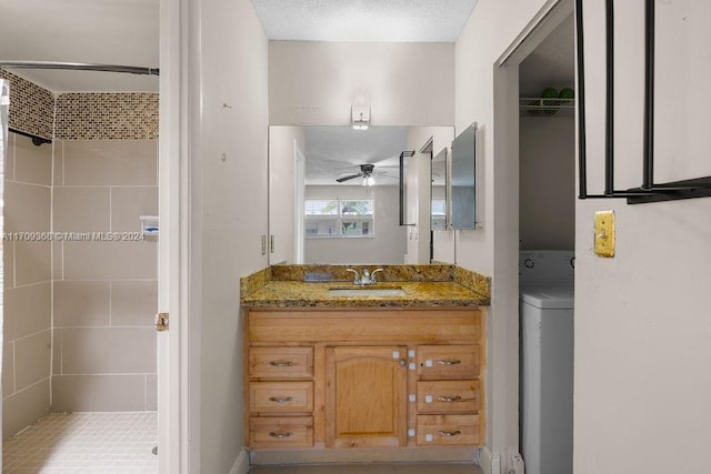 bathroom featuring a tile shower, vanity, a textured ceiling, ceiling fan, and washer / dryer