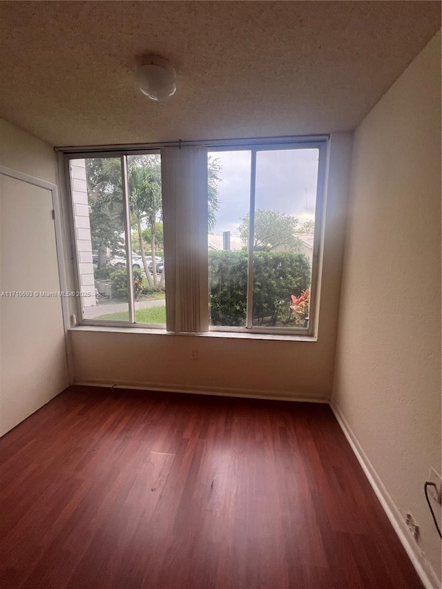 empty room with plenty of natural light, dark hardwood / wood-style floors, and a textured ceiling