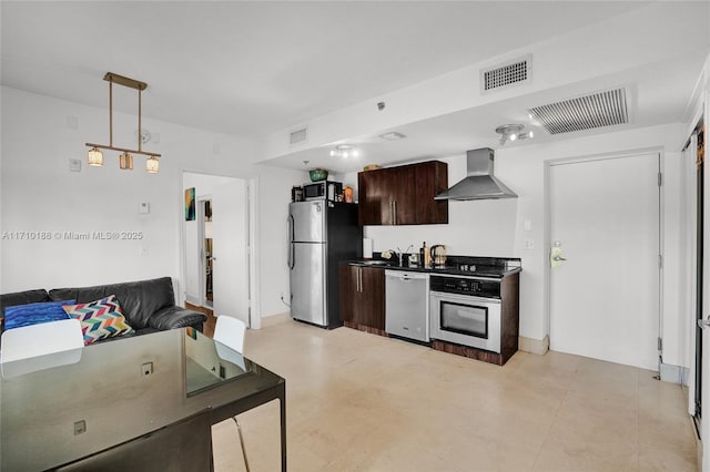 kitchen with wall chimney range hood, pendant lighting, sink, stainless steel appliances, and dark brown cabinets