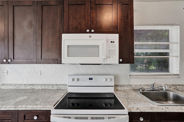 kitchen with dark brown cabinetry, white appliances, and sink