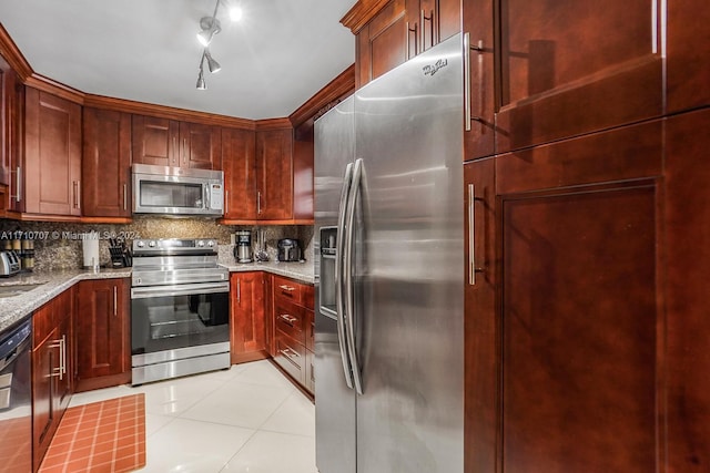 kitchen with appliances with stainless steel finishes, backsplash, light stone counters, and light tile patterned flooring