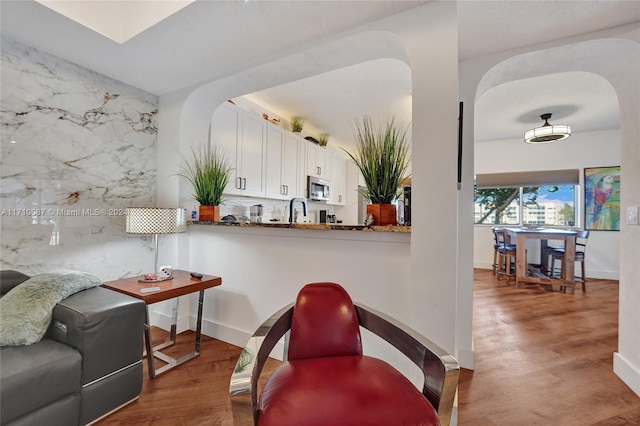 kitchen featuring sink, kitchen peninsula, stone countertops, dark hardwood / wood-style flooring, and white cabinetry