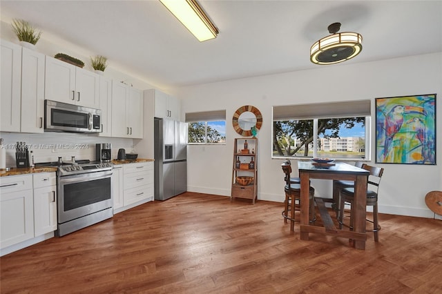 kitchen with white cabinets, dark stone countertops, dark hardwood / wood-style flooring, and stainless steel appliances