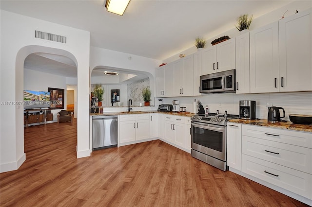 kitchen with appliances with stainless steel finishes, dark stone counters, sink, light hardwood / wood-style flooring, and white cabinets