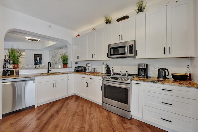 kitchen with dark stone counters, sink, light wood-type flooring, white cabinetry, and stainless steel appliances