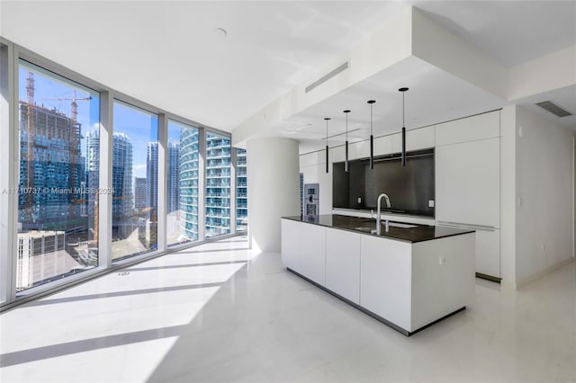 kitchen with white cabinetry, sink, a center island, a wall of windows, and decorative light fixtures