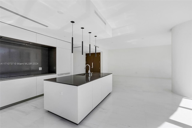 kitchen with pendant lighting, white cabinets, sink, and an island with sink