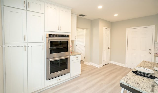 kitchen with light stone countertops, white cabinetry, stainless steel double oven, and light hardwood / wood-style floors