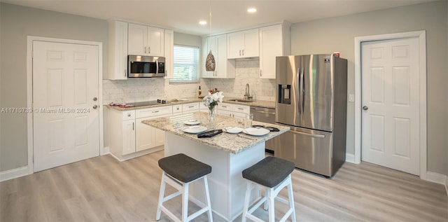 kitchen featuring white cabinets, appliances with stainless steel finishes, a kitchen island, and light stone countertops