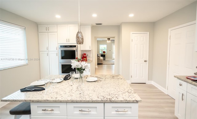 kitchen featuring ceiling fan, white cabinetry, double oven, pendant lighting, and light wood-type flooring