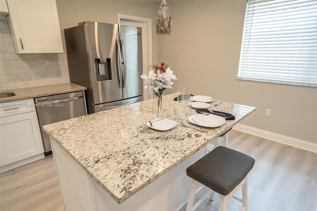 kitchen with white cabinetry, light stone countertops, a center island, stainless steel appliances, and tasteful backsplash