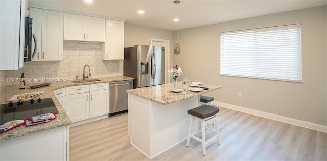 kitchen featuring white cabinetry, a center island, hanging light fixtures, stainless steel appliances, and light wood-type flooring