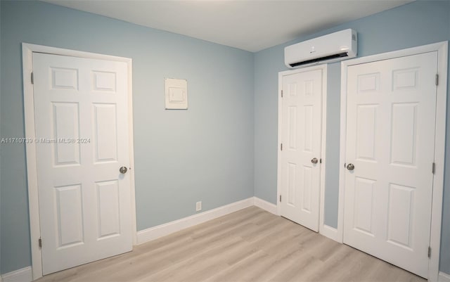 unfurnished bedroom featuring a closet, an AC wall unit, and light hardwood / wood-style flooring