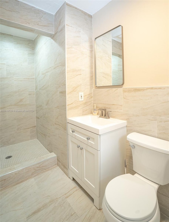 bathroom with tiled shower, vanity, tile walls, and toilet