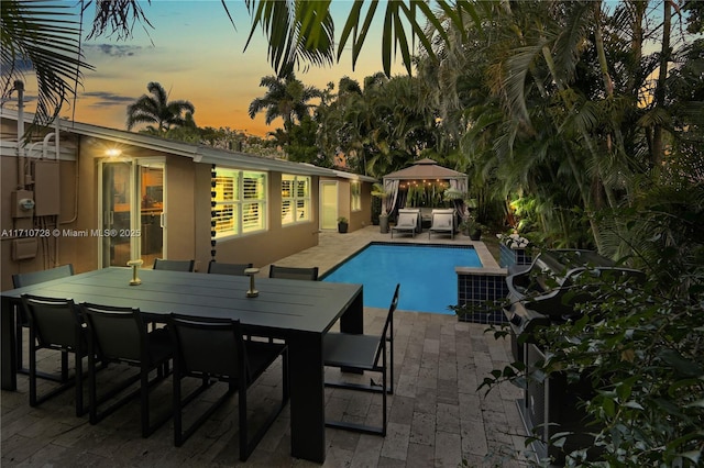 pool at dusk featuring a gazebo, outdoor dining space, a patio area, and an outdoor pool