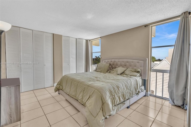 tiled bedroom featuring a wall of windows, a textured ceiling, and two closets