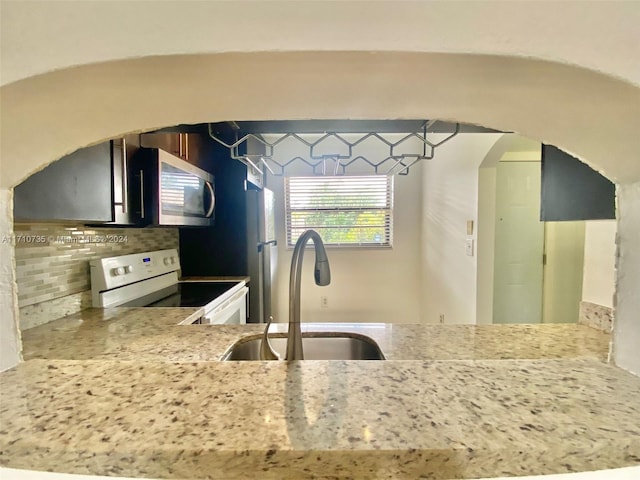 kitchen featuring kitchen peninsula, backsplash, light stone counters, white electric range oven, and sink