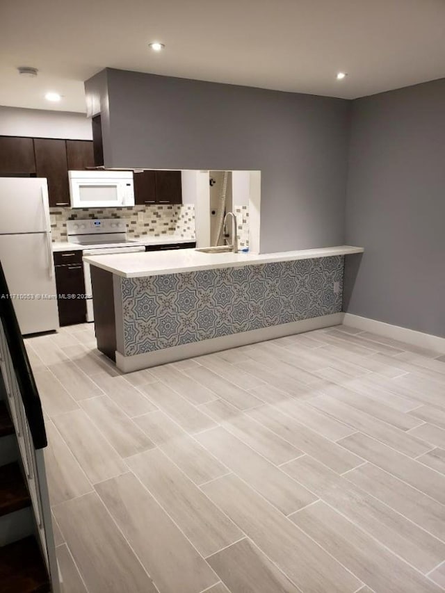 kitchen with sink, white appliances, tasteful backsplash, kitchen peninsula, and dark brown cabinetry