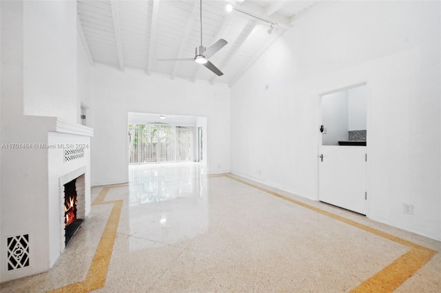 unfurnished living room featuring a fireplace, high vaulted ceiling, ceiling fan, and beamed ceiling