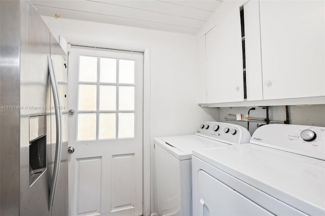 clothes washing area with washer and clothes dryer, cabinets, and plenty of natural light