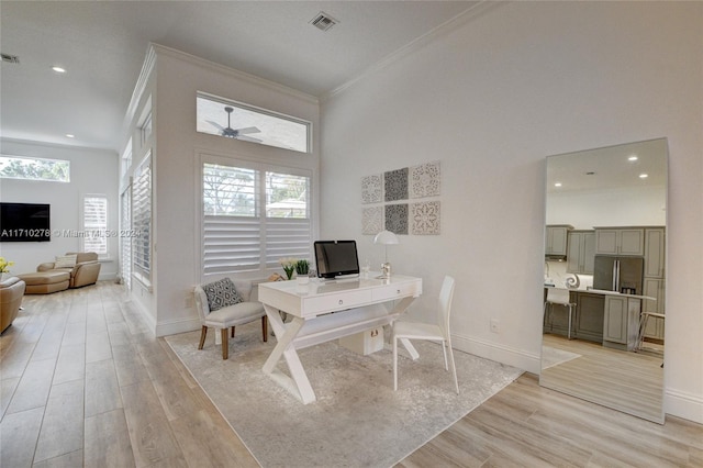 office space featuring crown molding, a towering ceiling, and light wood-type flooring