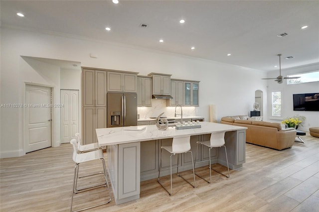 kitchen featuring a breakfast bar, stainless steel fridge with ice dispenser, light stone countertops, and a large island with sink