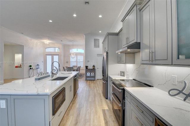 kitchen featuring light stone countertops, appliances with stainless steel finishes, a kitchen island with sink, sink, and gray cabinets