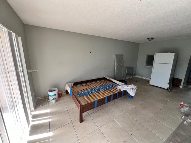 bedroom featuring white fridge, light tile patterned flooring, and a textured ceiling