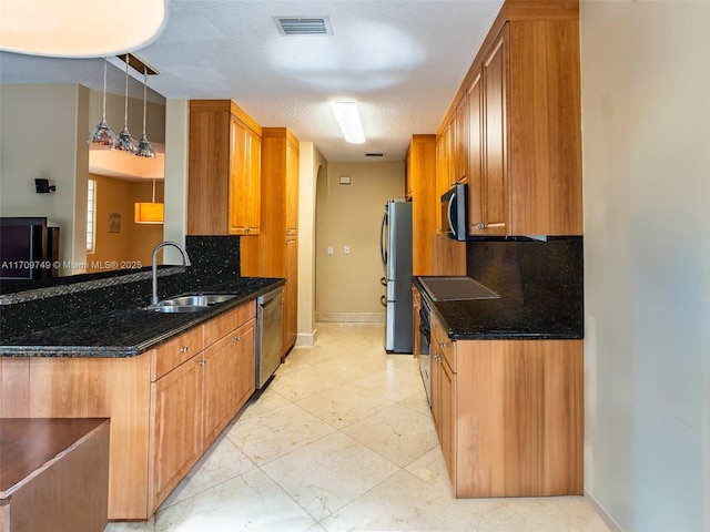 kitchen featuring decorative light fixtures, stainless steel appliances, dark stone counters, tasteful backsplash, and sink