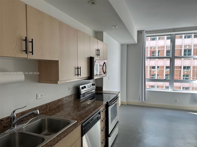 kitchen featuring appliances with stainless steel finishes, dark stone countertops, a healthy amount of sunlight, and sink