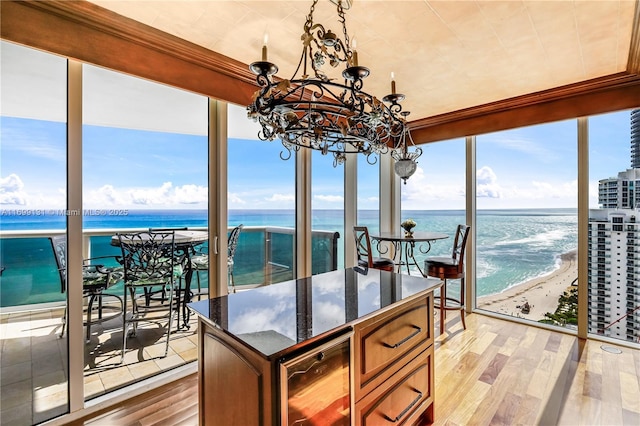 sunroom / solarium featuring an inviting chandelier, a view of the beach, a water view, plenty of natural light, and beverage cooler