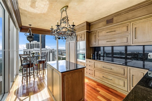 kitchen with backsplash, light hardwood / wood-style flooring, dark stone countertops, black electric cooktop, and decorative light fixtures