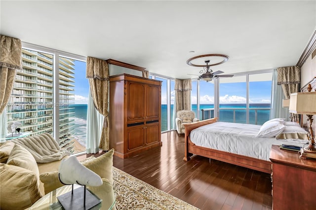 bedroom with expansive windows, a water view, dark wood-type flooring, and multiple windows