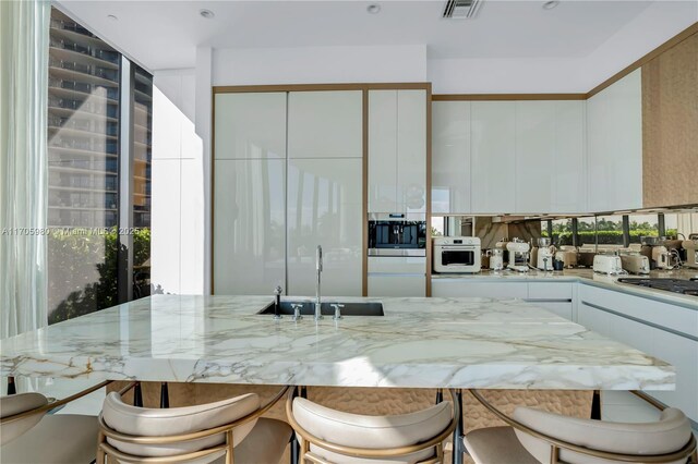 kitchen with sink, light tile patterned floors, a breakfast bar area, a center island with sink, and white cabinets