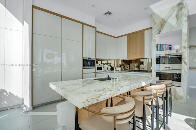 kitchen featuring white cabinets, a spacious island, sink, light tile patterned flooring, and stainless steel appliances