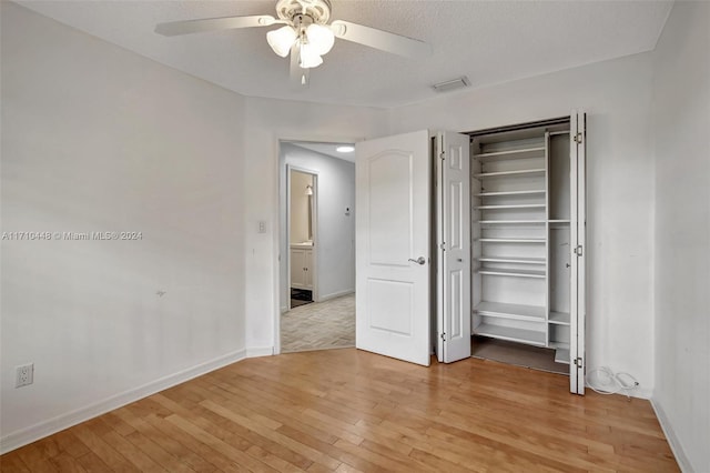 unfurnished bedroom featuring ceiling fan, a closet, a textured ceiling, and light wood-type flooring