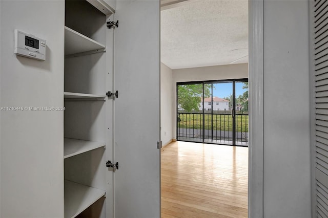 hall featuring light wood-type flooring and a textured ceiling