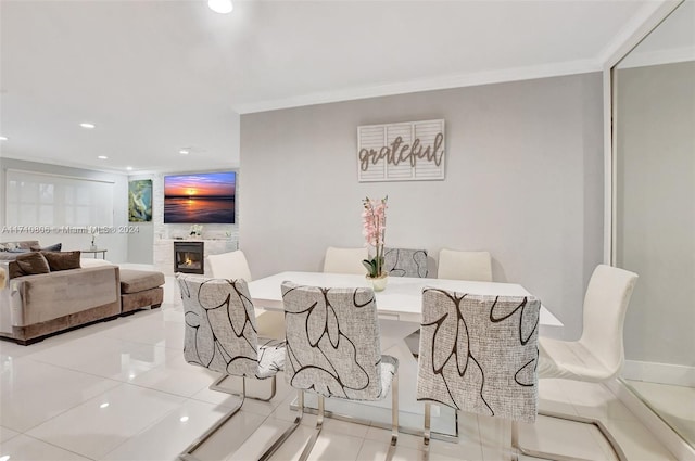 dining area featuring a large fireplace, light tile patterned floors, and ornamental molding