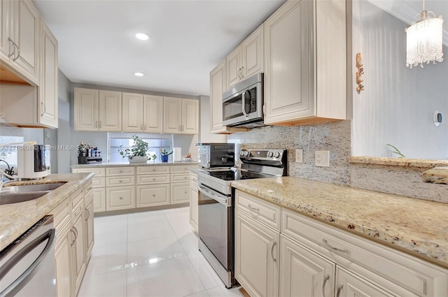 kitchen with sink, hanging light fixtures, light tile patterned floors, appliances with stainless steel finishes, and light stone counters