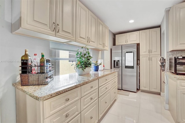 kitchen featuring cream cabinetry, light tile patterned flooring, light stone countertops, and stainless steel fridge with ice dispenser