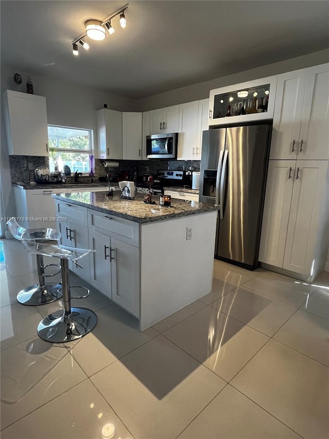 kitchen featuring light tile patterned floors, stainless steel appliances, white cabinetry, and a center island with sink