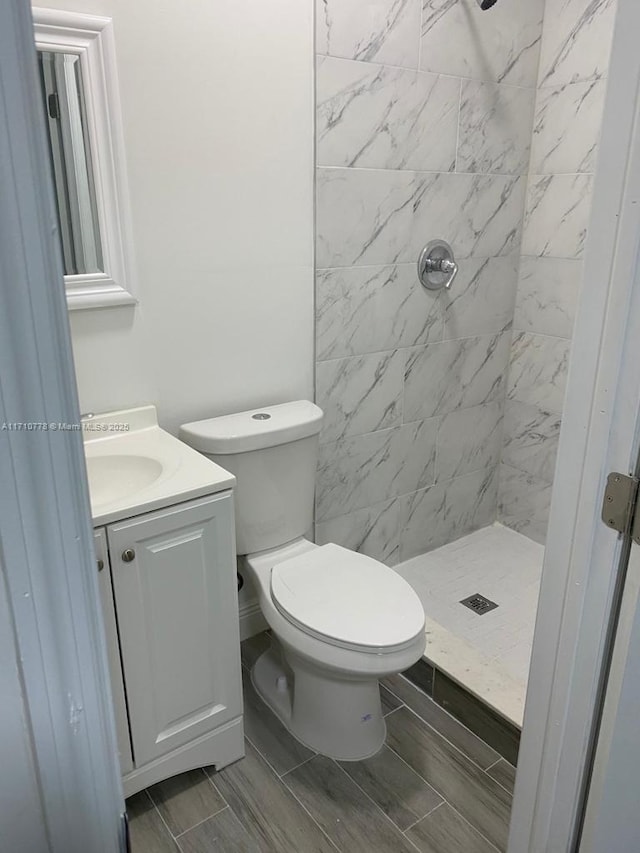 bathroom with toilet, a tile shower, and vanity