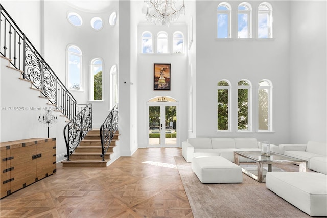 entryway featuring french doors, a towering ceiling, an inviting chandelier, and light parquet flooring