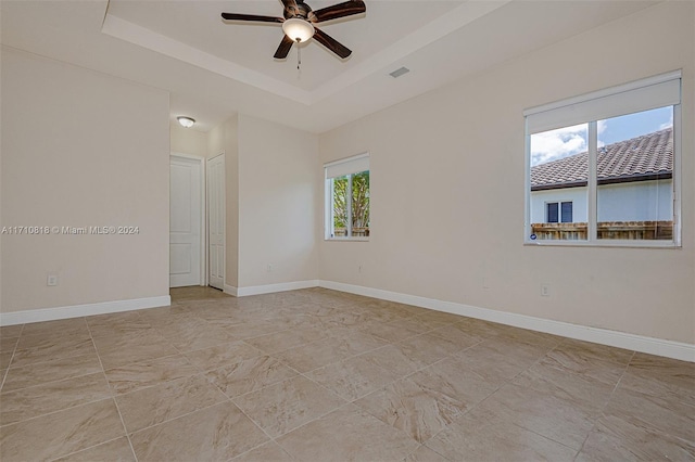 unfurnished room featuring plenty of natural light, ceiling fan, and a raised ceiling