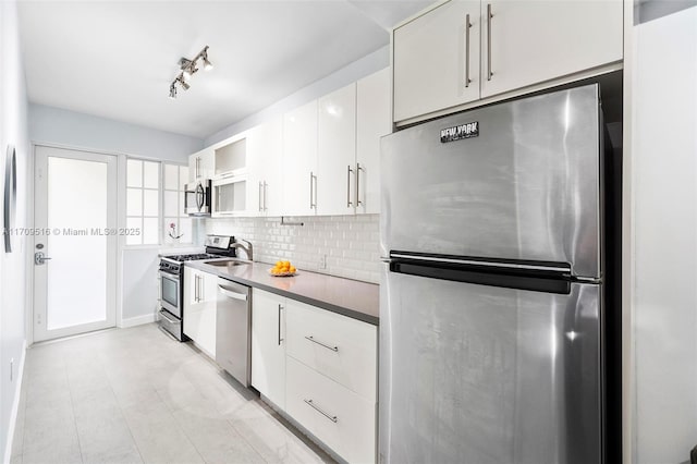 kitchen with track lighting, white cabinets, sink, decorative backsplash, and stainless steel appliances