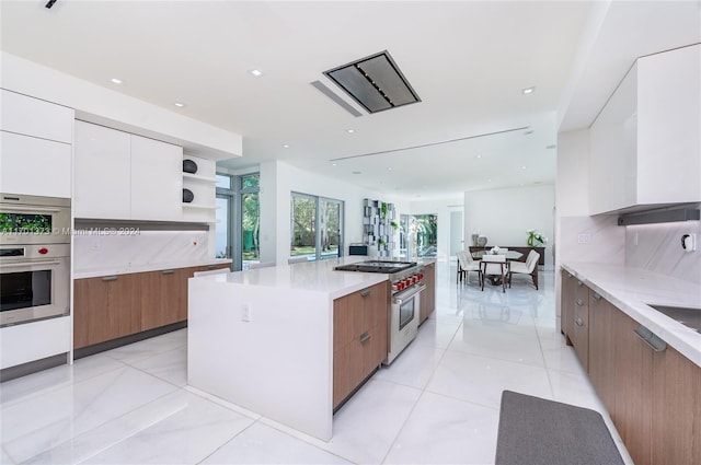 kitchen with a center island, decorative backsplash, light tile patterned floors, appliances with stainless steel finishes, and white cabinetry