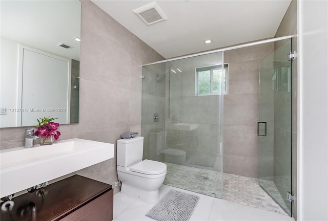 bathroom with tile patterned floors, toilet, a shower with door, vanity, and tile walls