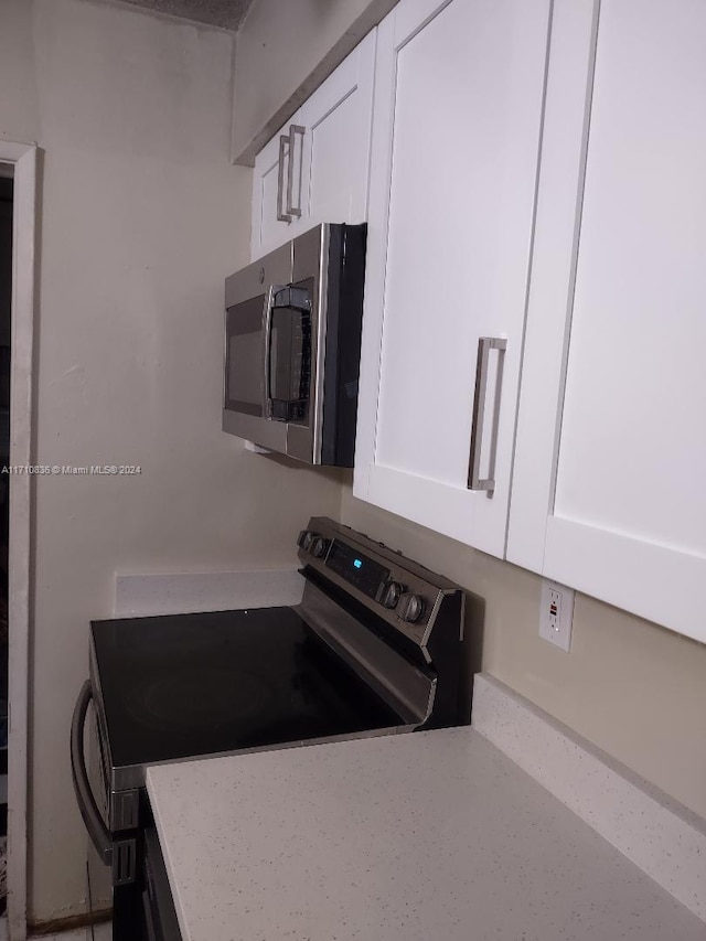 kitchen featuring white cabinets, light stone countertops, and black range with electric stovetop