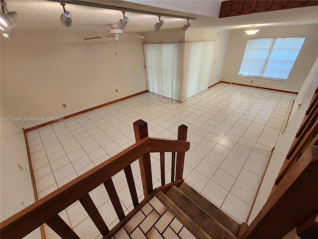 stairway with a textured ceiling, track lighting, tile patterned floors, and ceiling fan